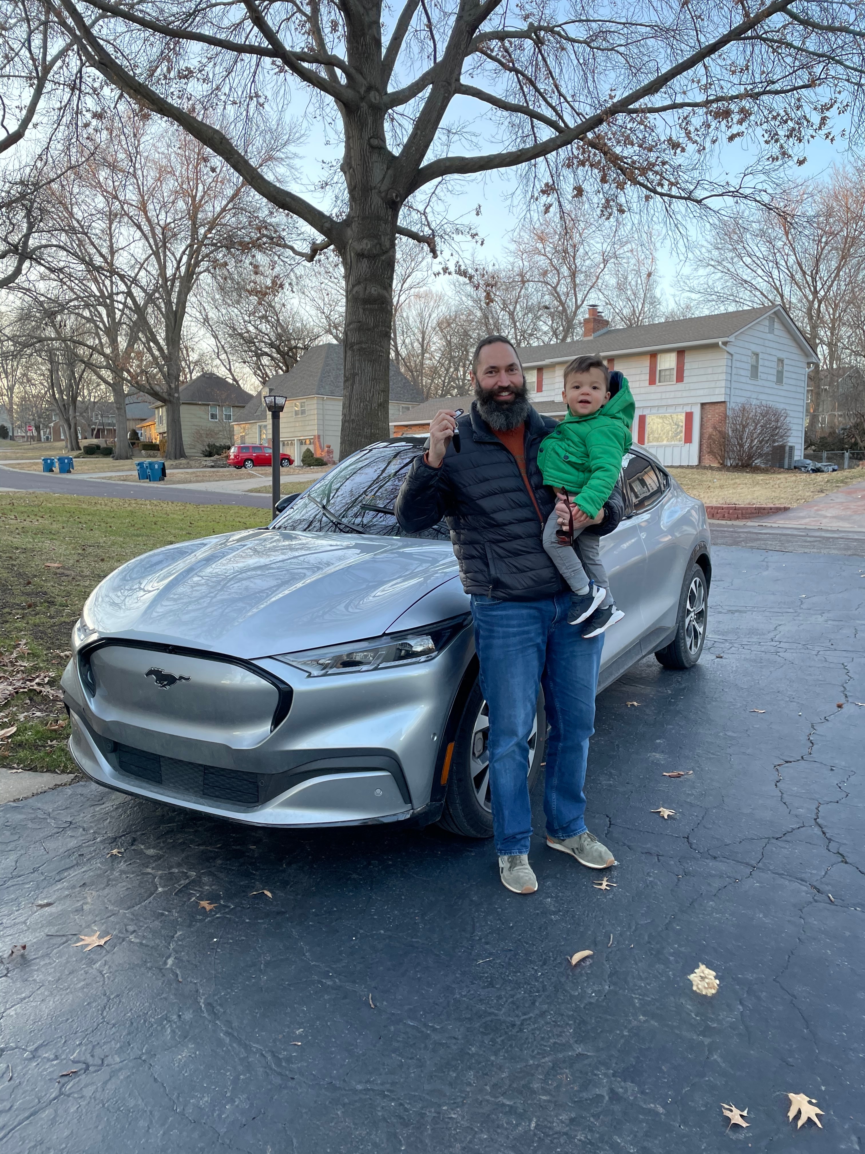Clayton holding Oliver while posing in front of the Mustang Mach-E.